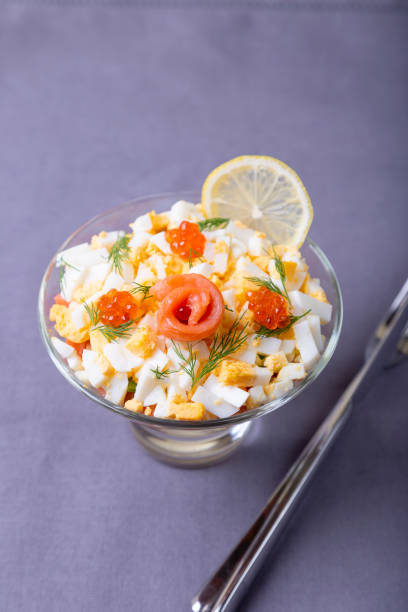 Puff salad with lightly salted trout (salmon), caviar, egg and vegetables. A traditional dish, one serving in a glass glass on a gray background. Croup