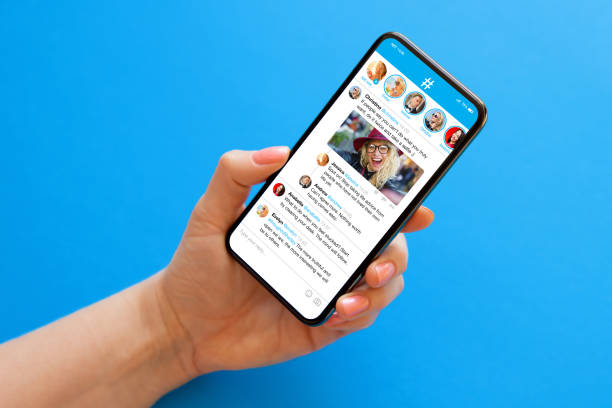 pessoa segurando celular na mão em fundo azul com amostra de aplicativo de microblogs de mídia social na tela - microblog - fotografias e filmes do acervo