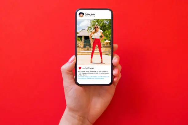Photo of Woman holding phone in hand with photo of fashion model in red pants on red background