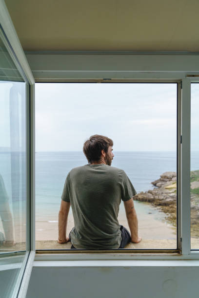 istock Back view of unrecognizable man sit on a window frame looking at the sea. 1358932431