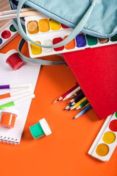 istock A blue backpack with different colored stationery, paints on an orange background. Banner for a children's art club or school 1358932645