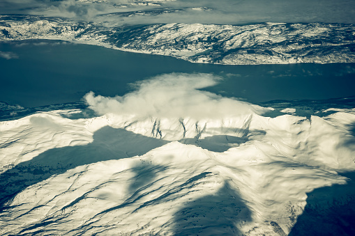 Aerial view from an airplane flying high over the snow covered mountains in Northern Norway during a beautiful winter day.