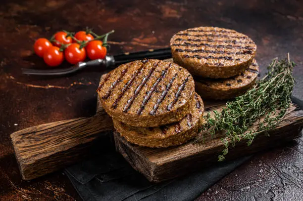 BBQ Grilled plant based meat burger patties,  vegan cutlets on wooden board with herbs. Dark background. Top view.