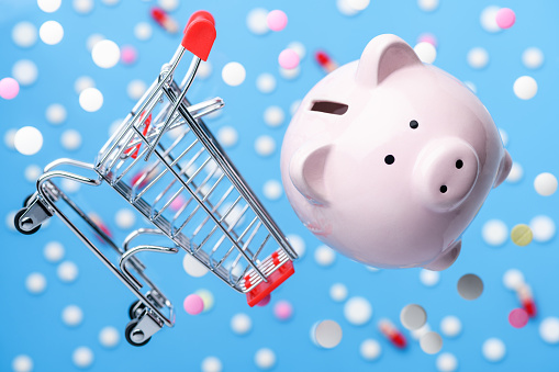 Flying piggy Bank and levitation shopping trolley cart on the blue background of pills and tablets. Medicine and healthcare concept. Drug delivery