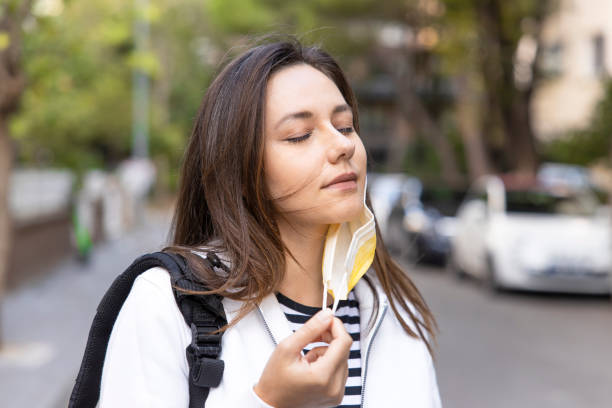 Young woman relieving taking off mask to breath fresh air in street stock photo