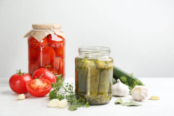 istock Glass jars of pickled cucumbers and tomatoes on white table 1358944145