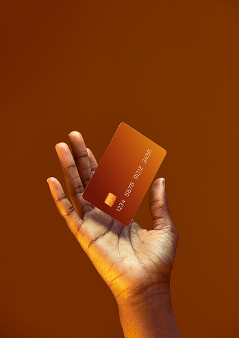 Mano femenina afroamericana sostiene plantilla levitante Tarjeta de crédito bancaria con servicio en línea sobre fondo naranja dorado photo