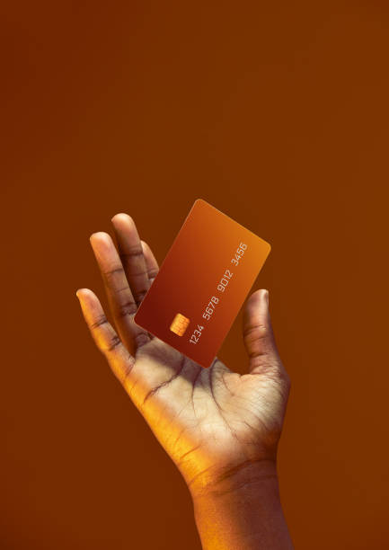 mano femminile afroamericana tiene il modello levitante carta di credito bancaria con servizio online su sfondo arancione dorato - carta di credito foto e immagini stock