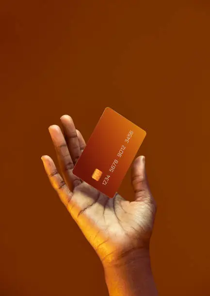African american female hand holds levitating template Bank credit card with online service on golden orange background. High quality photo