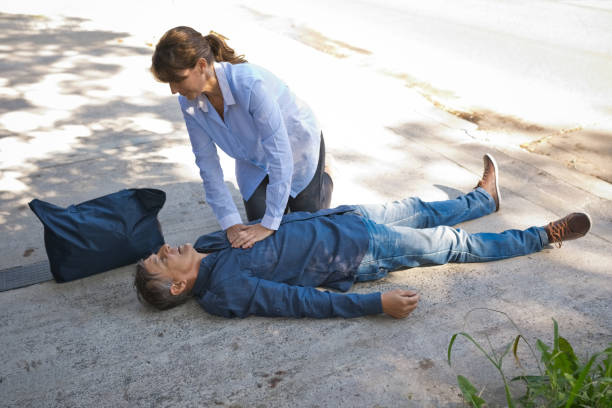 mujer dando primeros auxilios a un hombre mayor - human hand help pain heart attack fotografías e imágenes de stock