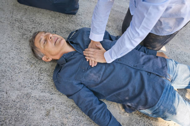 Woman giving first aid to a senior man Woman using hand pump on chest for first aid emergency on heart attack. Unconscious senior man lying on asphalt. cpr stock pictures, royalty-free photos & images