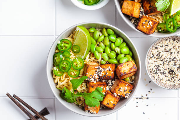 zuppa di ramen di noodles vegani con tofu marinato, fagioli edamame e peperoncino piccante in ciotole grigie. - cooked soup food bowl foto e immagini stock