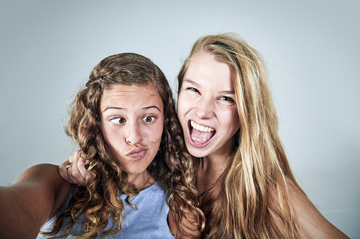 Squnting puckering young woman and happy laughing teenage girl taking a self-portrait photograph.