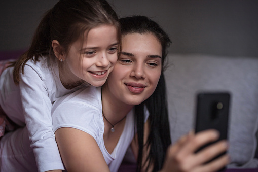 Close up of cheerful siblings hugging and taking a selfie together at home