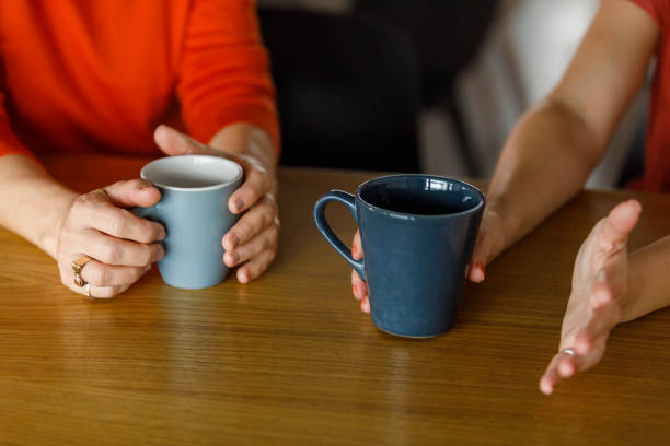 istock Two women sitting at table, chatting, having coffee together 1358951397