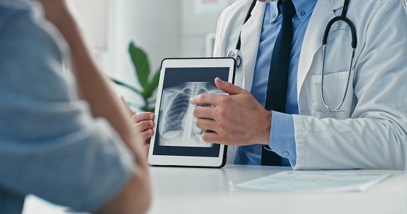 Foto recortada de un médico irreconocible sentado con su paciente y mostrando sus radiografías en una tableta digital photo