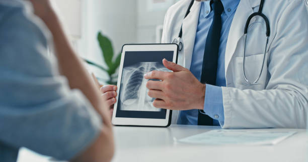 Cropped shot of an unrecognisable doctor sitting with his patient and showing her x-rays on a digital tablet stock photo