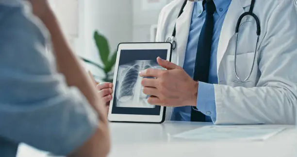 Photo of Cropped shot of an unrecognisable doctor sitting with his patient and showing her x-rays on a digital tablet