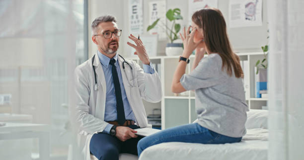 Shot of a mature doctor sitting with his patient in the clinic and asking questions during a consultation stock photo