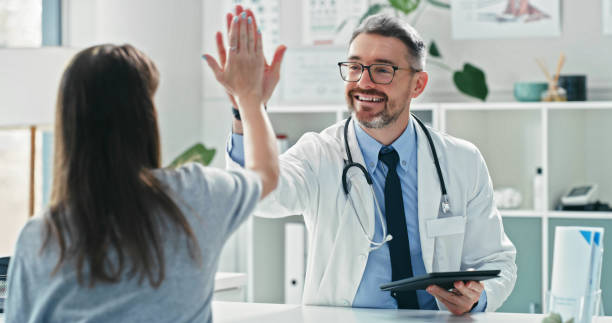 Shot of a mature doctor sitting with his patient and giving her a high five during a consultation stock photo