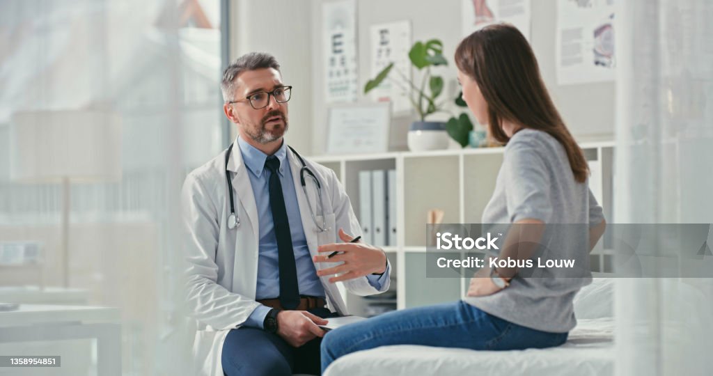 Shot of a mature doctor sitting with his patient in the clinic and asking questions during a consultation I get really bad tummy cramps Irritable Bowel Syndrome Stock Photo