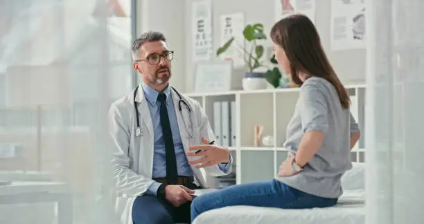 Photo of Shot of a mature doctor sitting with his patient in the clinic and asking questions during a consultation