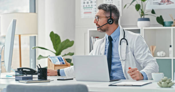 istock Shot of a mature doctor sitting alone and using his computer while wearing a headset during an online consultation 1358954978