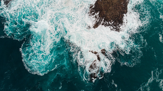 A top view on a the edge of an archipelago with crashing waves with a beautifully dark aquamarine color of the sea or the ocean