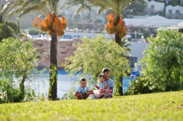 istock Three kids sitting on grass at Turkey resort against palms. 1358964800