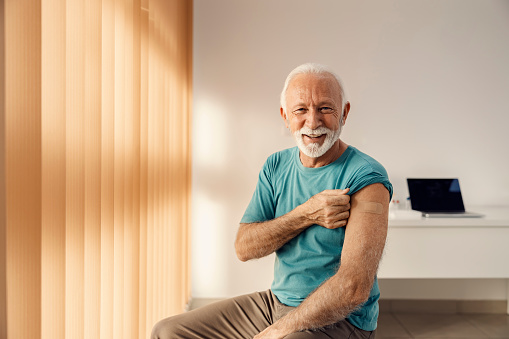 Vacunación para ancianos. Un anciano feliz sentado en el consultorio del médico y mostrando su brazo con yeso adhesivo después de la vacuna covid 19. photo