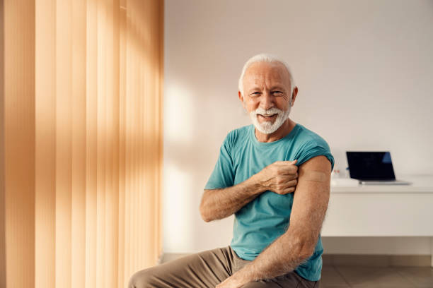 Vaccination for elders. A happy senior man sitting in the doctor's office and showing his arm with adhesive plaster after covid 19 vaccine. Vaccination for elders. A happy senior man sitting in the doctor's office and showing his arm with adhesive plaster after covid 19 vaccine. coronation photos stock pictures, royalty-free photos & images