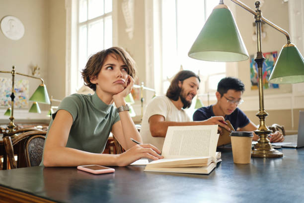 istock Young female student with book thoughtfully working on study project in library of university 1358966386
