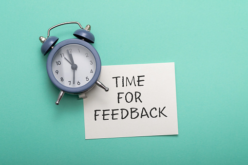 blue alarm clock lies on a blue background next to a card with the text time for feedback. Conceptual business photo on the topic of product evaluation and customer reviews.