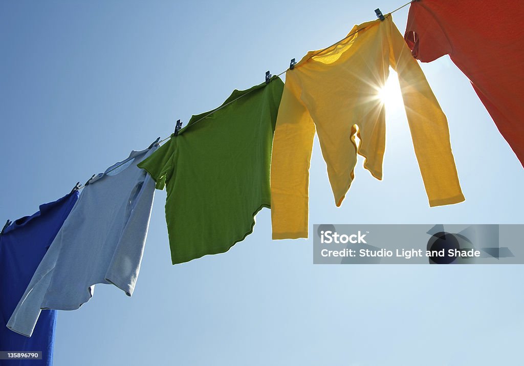 Abiti colorati su una linea lavanderia e sole splendente - Foto stock royalty-free di Stendino