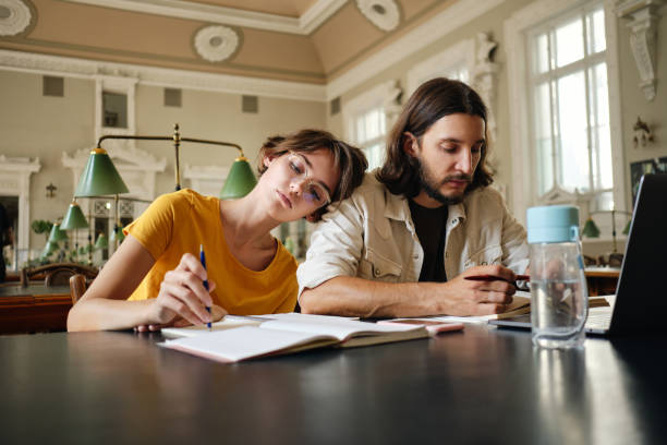istock Two tired students wearily working on study project with laptop and books in library of university 1358967914