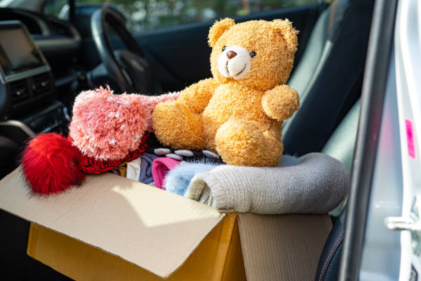Volunteer woman provide clothing donation box with used clothes and doll at home to support help for refugee, homeless or poor people in the world. stock photo