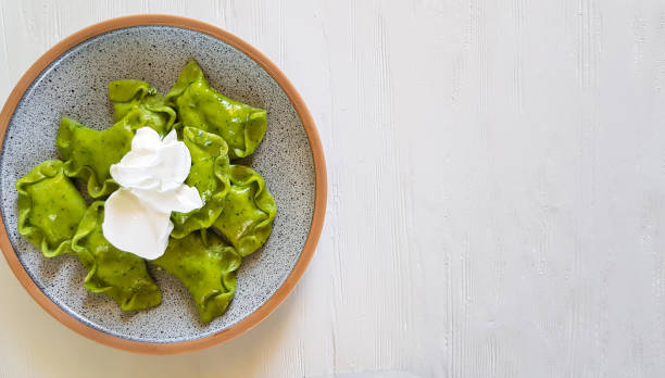 istock Green dumplings with cottage cheese, spinach and sour cream on ceramic plate on white background 1358968927