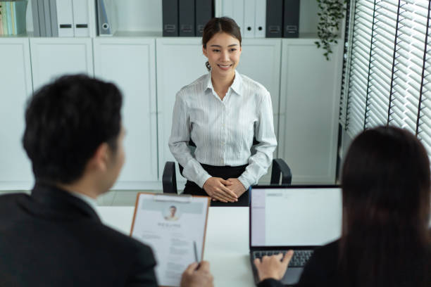 Asian beautiful woman talk with hr manager for job interview in office. Attractive female sit on table and give resume to human resources managers business recruit people for apply job at workplace. stock photo