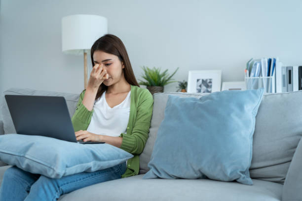 istock Exhausted Asian business woman hurt eye while using laptop computer. Young girl office worker sit on sofa feel visual fatigue and eye strain tired from overwork and massage dry irritable eye at home. 1358970504