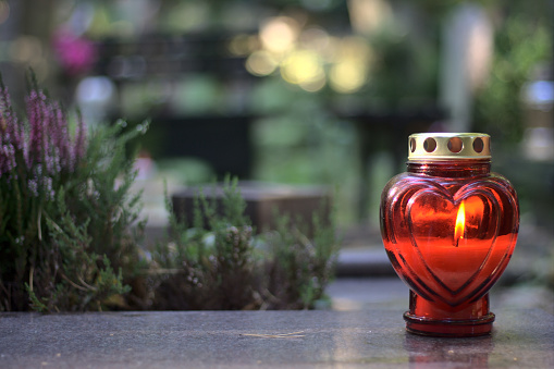 A red heart - shaped candle (snitch) on a tombstone in a cemetery during the day. All Saints' Day, copy space.