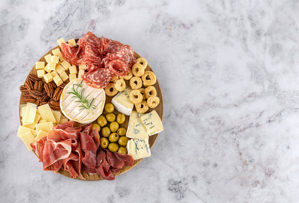 Top view of tasty charcuterie board with cheese, grape, nuts, olives, and ham on a circle kitchen plate Top view of tasty charcuterie board with cheese, grape, nuts, olives, and ham on a circle kitchen plate on the marble stone background, top view, copy space. Gourmet food, copy space. charcuterie stock pictures, royalty-free photos & images