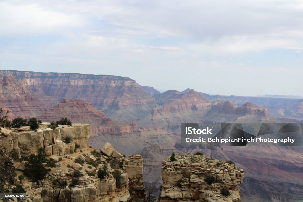 View of the Grand Canyon Looking Across Under Cloudy Sky Broad view landscape shot of the Grand Canyon with vibrant layers in the canyon under a cloudy sky with cliffs in the foreground and the far rim of the canyon on the horizon. Arizona Stock Photo