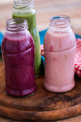 Fresh made green, pink and purple smoothies in small bottles on table,  close-up, no people