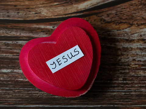 Red heart with the handwritten name Jesus on wooden table background. The Christian biblical concept of love, faith, and hope in Christ, our God, and LORD. Top view.