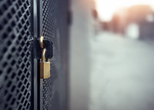 Caged in commercial or residential area. Golden metal lock on black fence with reinforced mesh. Safety backdrop texture. Defocused street background Selective focus.