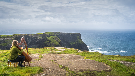 Doolin, Ireland, August 2019 Woman playing harp on the top of iconic Cliffs of Moher, popular tourist attraction, Wild Atlantic Way, County Clare