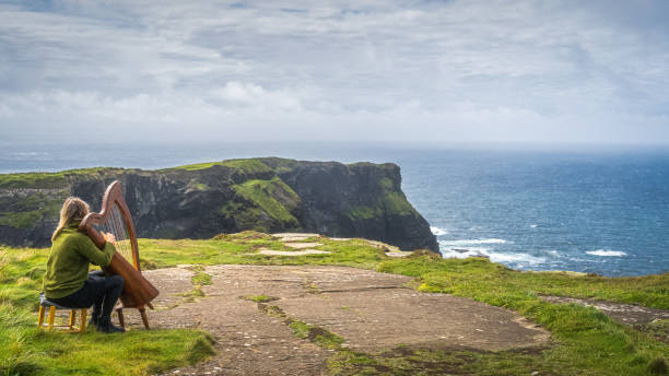 Woman playing harp on the top of iconic Cliffs of Moher, Ireland Doolin, Ireland, August 2019 Woman playing harp on the top of iconic Cliffs of Moher, popular tourist attraction, Wild Atlantic Way, County Clare doolin photos stock pictures, royalty-free photos & images