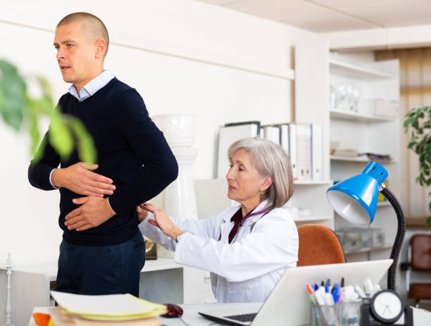 Senior woman nephrologist examining patient complaining of kidneys pain Focused senior woman nephrologist examining worried patient complaining of kidneys pain sitting at table in medical office anamnesis stock pictures, royalty-free photos & images