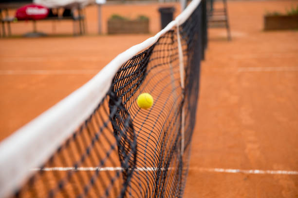 Tennis net on red clay court with lines and shadows