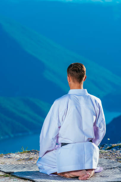 istock Karate master meditating on top of a mountain wearing kimono while looking down at the mountain lake. 1358991976